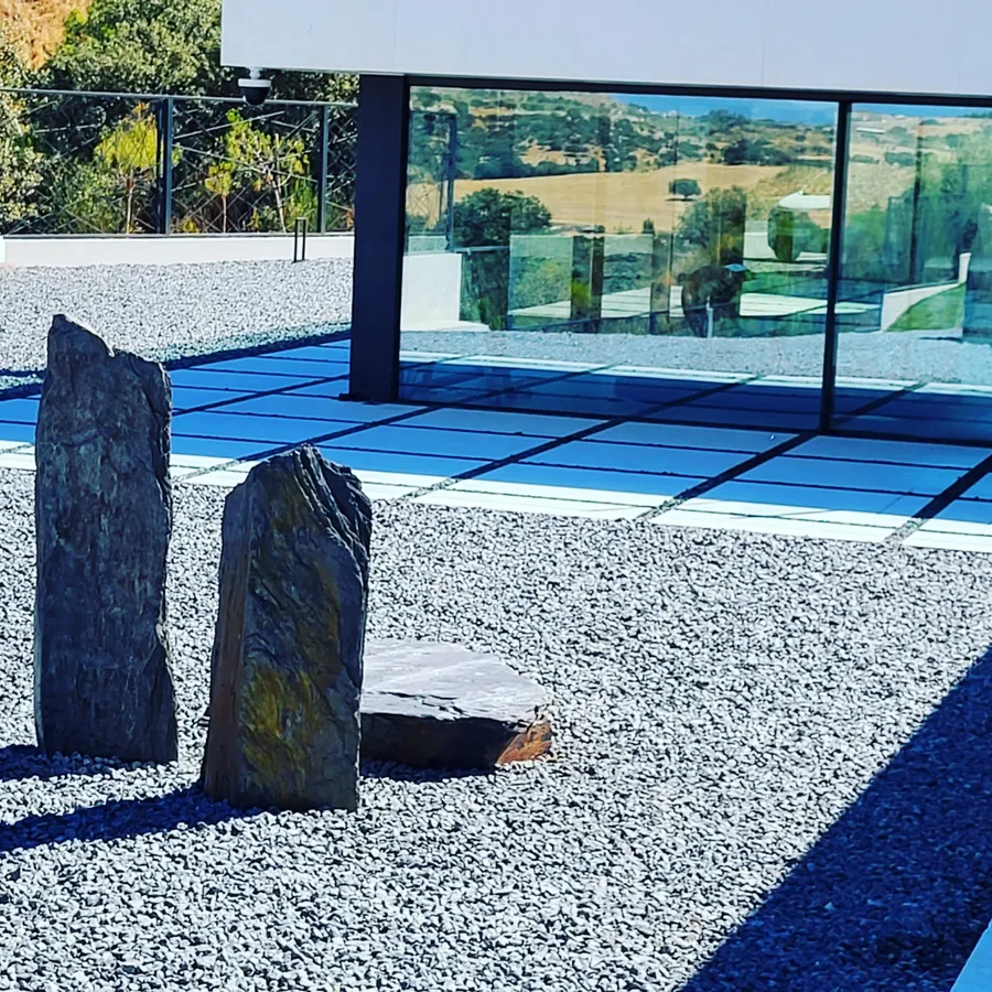 Jardín de grava con monolito de piedra y piscina al fondo