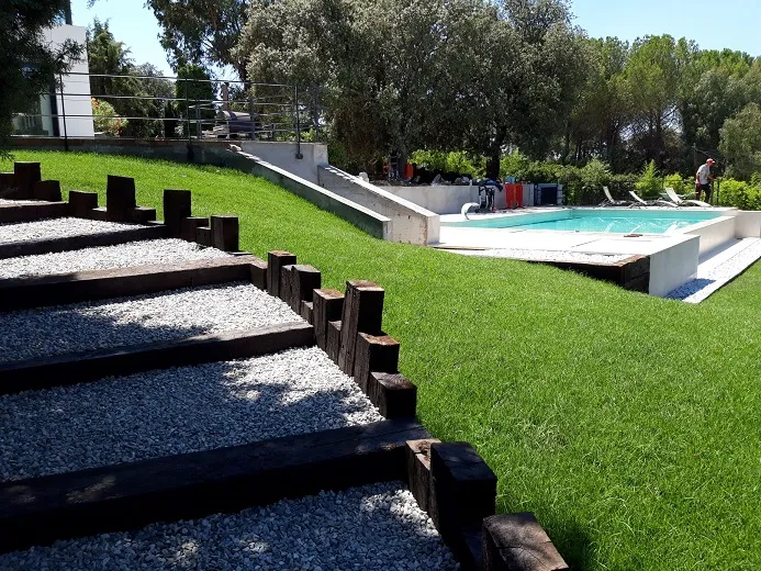 Jardín con escalera de traviesas y grava, y la piscina al fondo