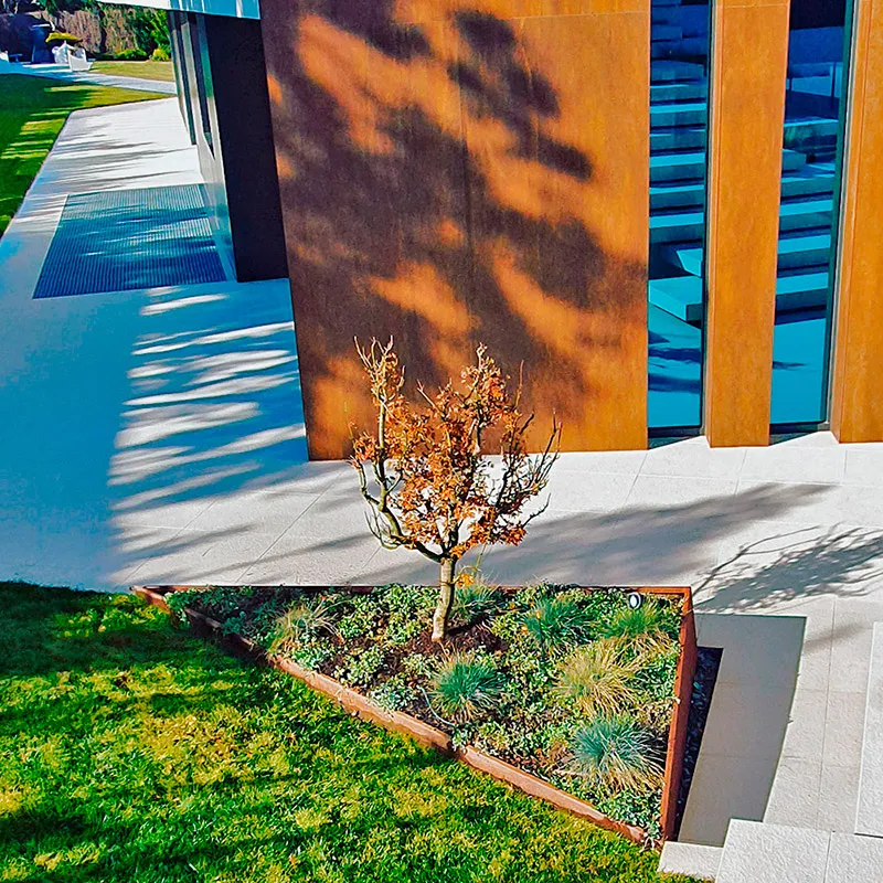 Parterre con un árbol joven junto a una fachada de madera y metal